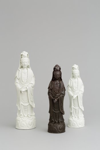 Foto, chinesiche Guanyin aus Porzellan neben zwei kleineren, Meissener Nachbildungen aus Böttgersteinzeug und Porzellan