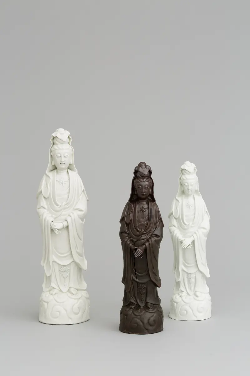 Foto, chinesiche Guanyin aus Porzellan neben zwei kleineren, Meissener Nachbildungen aus Böttgersteinzeug und Porzellan