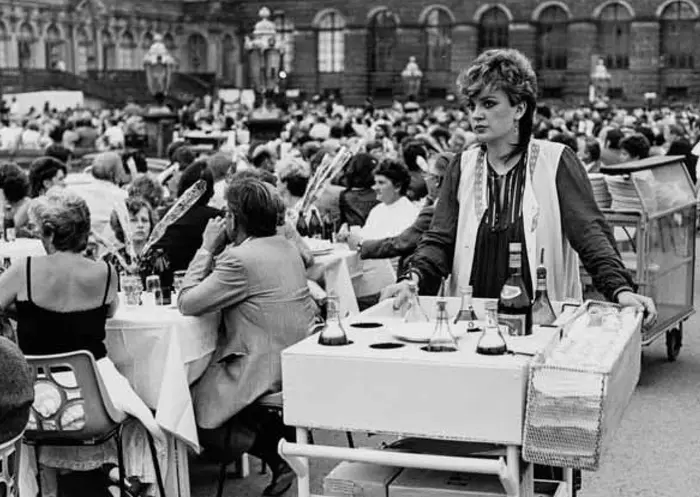 Schwarz-Weiß-Fotografie einer Veranstaltung im Schlosshof, im Vordergrund ist eine Frau mit Servierwagen zu sehen.